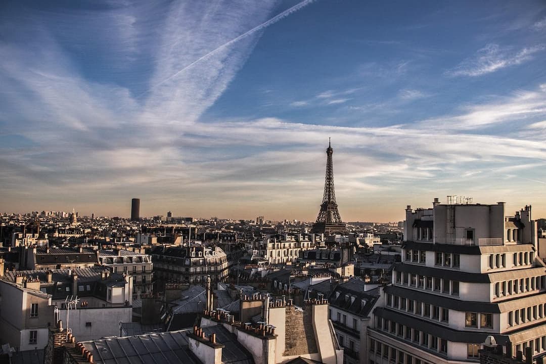 Vue panoramique de Paris avec la tour Eiffel et les toits haussmanniens sous un ciel bleu strié de nuages.