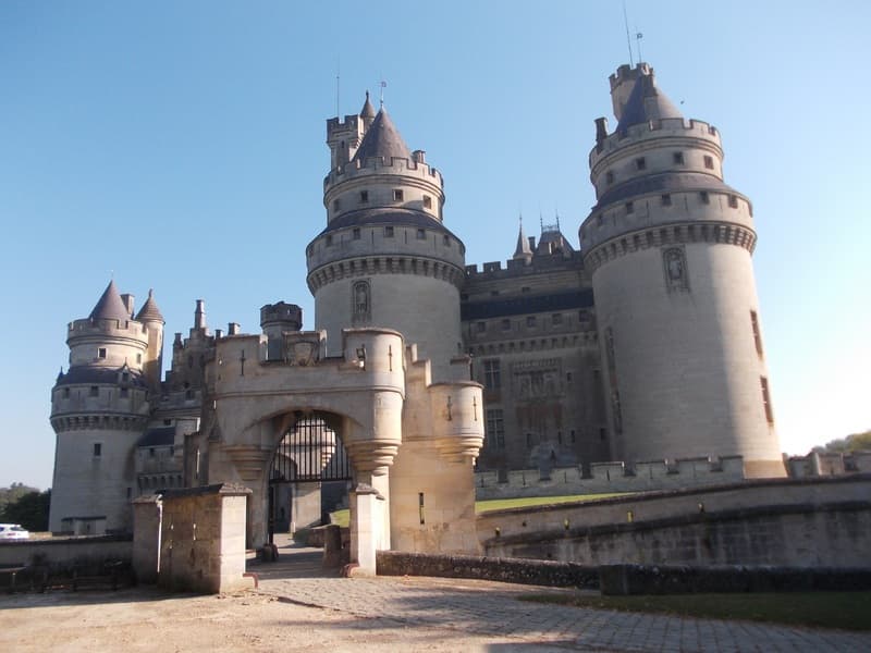 Château de Pierrefonds avec ses tours majestueuses et son entrée fortifiée, sous un ciel bleu éclatant en France.