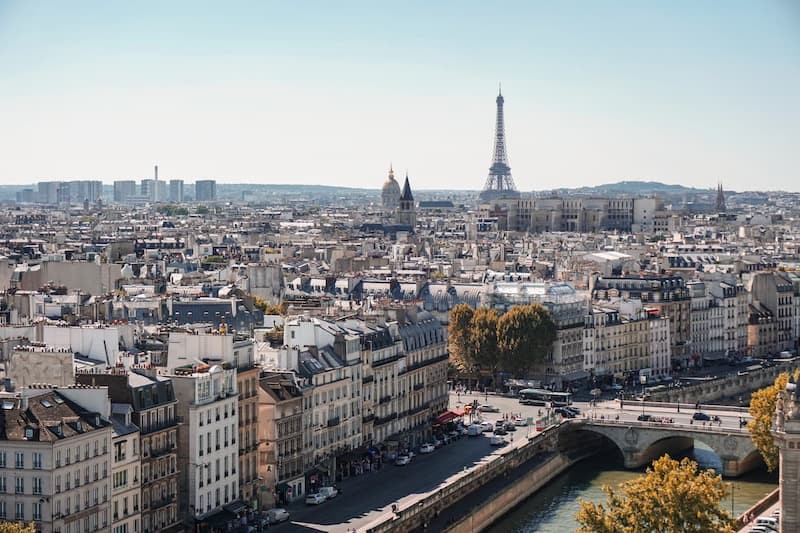 Vue panoramique de Paris avec la Tour Eiffel dominant les toits haussmanniens et la Seine traversée par un pont en pierre