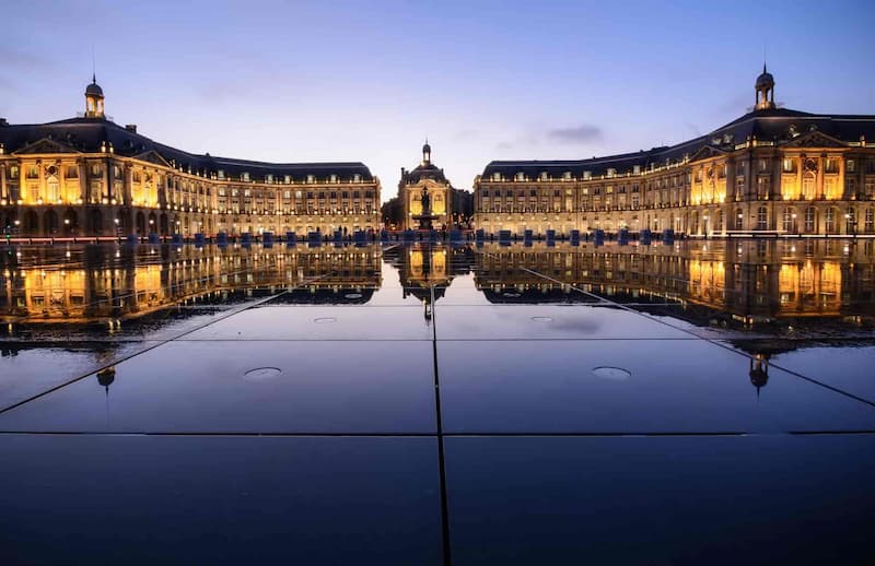 Place de la Bourse à Bordeaux la nuit, bâtiments historiques illuminés se reflétant dans l'eau miroir