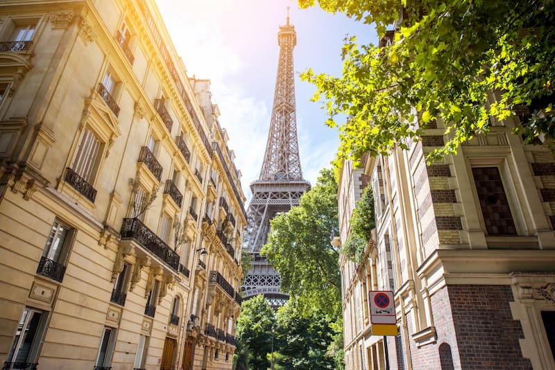 Tour Eiffel vue depuis une rue bordée d’immeubles et d’arbres à Paris.