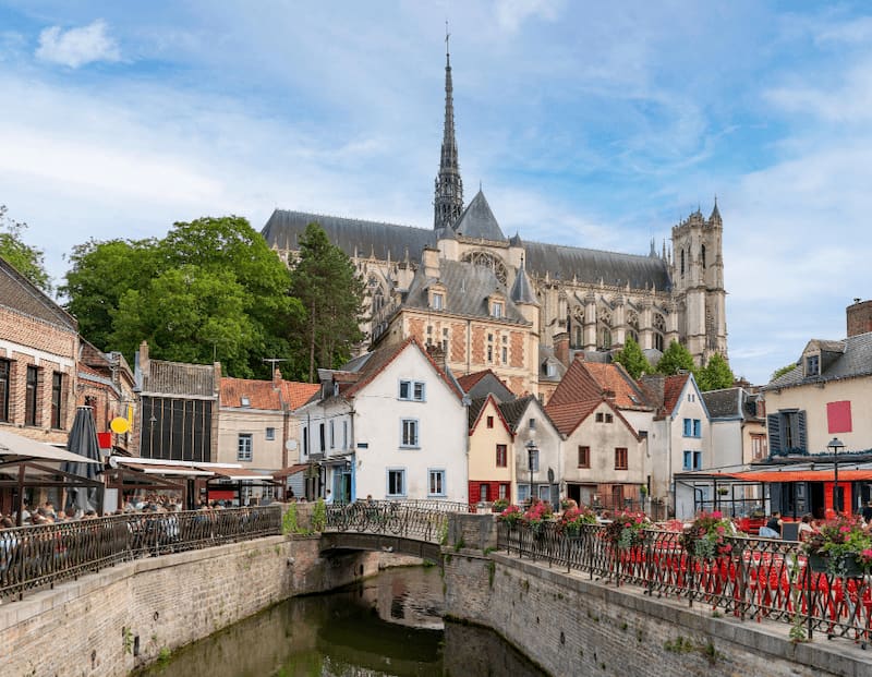 Vue de la cathédrale d’Amiens dominant les maisons colorées du quartier Saint-Leu et un canal fleuri au premier plan