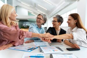 Quatre expertes-comptables unissant leurs mains au-dessus de documents financiers, symbolisant un rapprochement de cabinets comptables