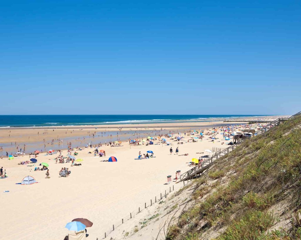 Plage de Mimizan animée avec dunes, parasols et océan Atlantique.