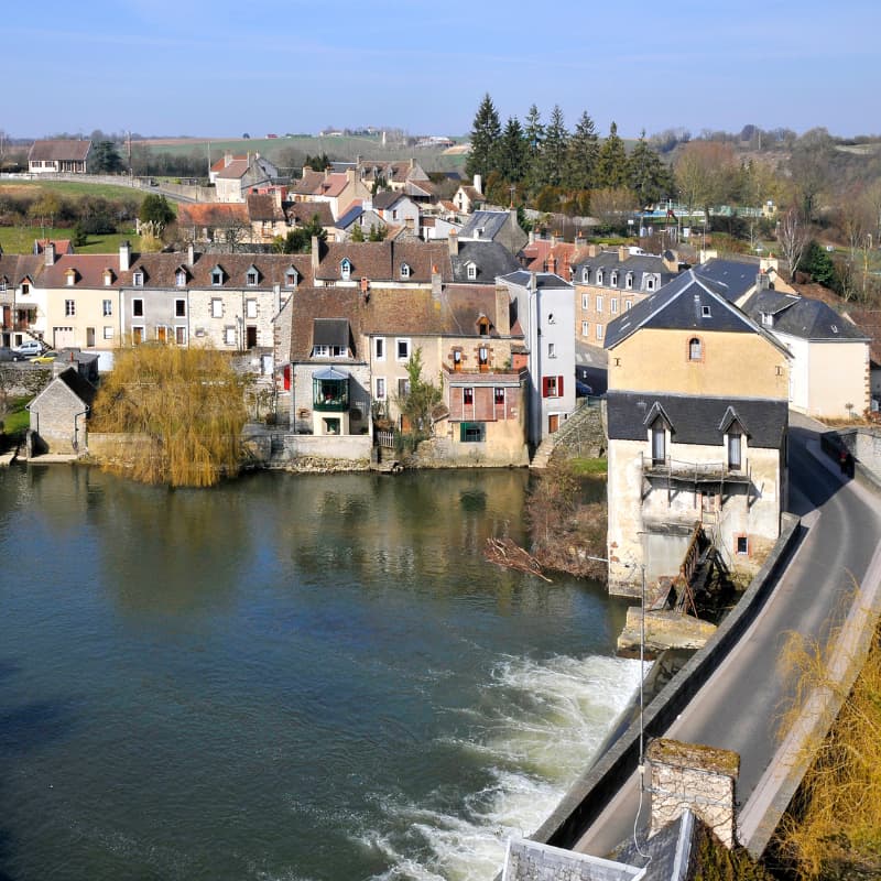 Vue sur un village de la Sarthe avec maisons anciennes en bord de rivière, pont et ancien moulin.