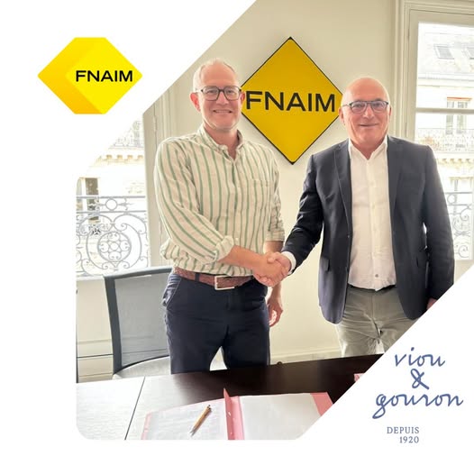 Poignée de main entre Mathieu PUICHAULT, de Viou & Gouron, et Loïc CANTIN, de la FNAIM devant le logo FNAIM, partenariat immobilier Viou & Gouron.